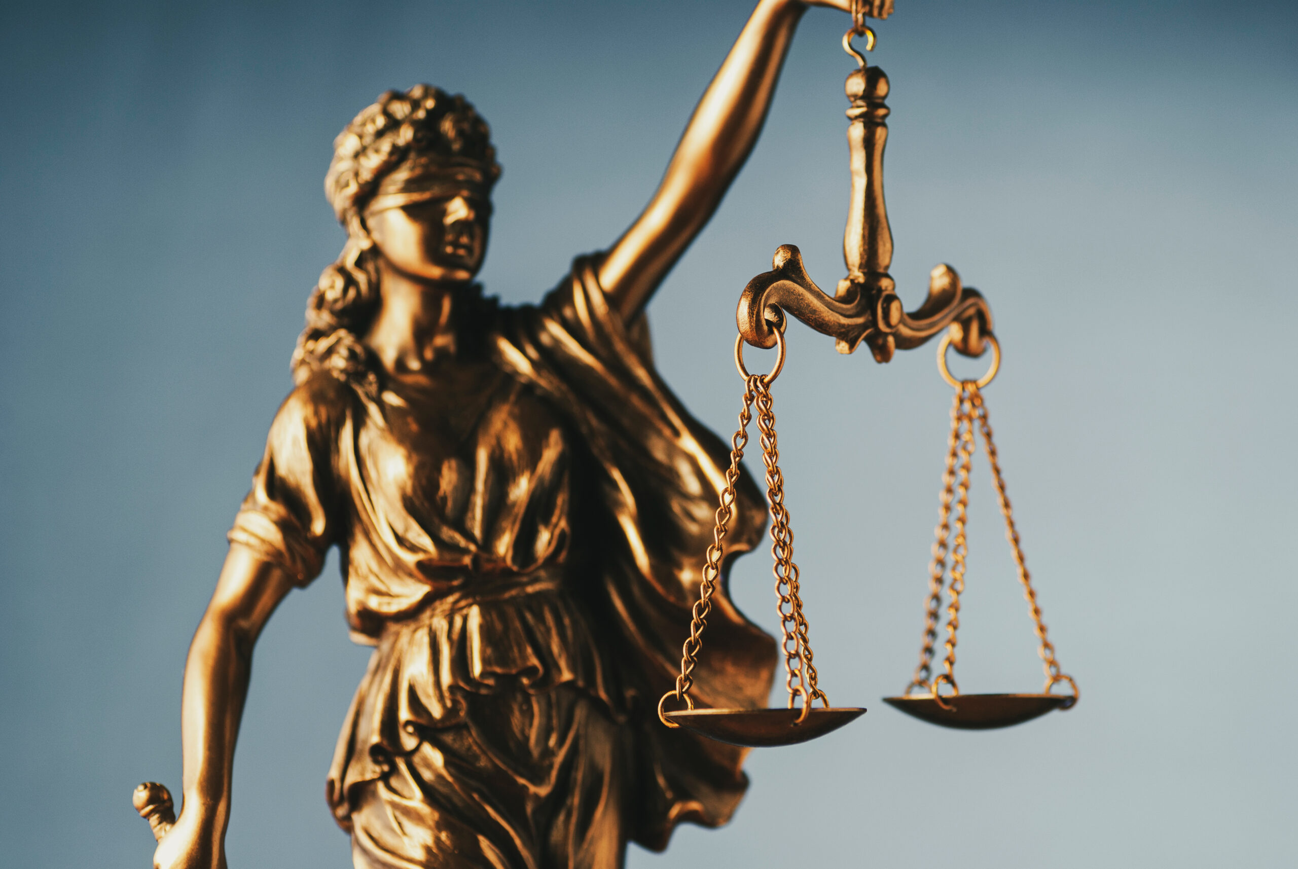 Bronze statue of Justice wearing a blindfold and holding scales symbolic of the law over a grey background and copy space in a conceptual image